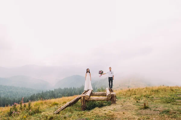 Bruidspaar op de houten brug. Mistige dag op bergen — Stockfoto