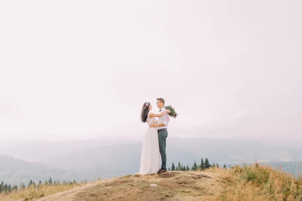 La novia y el novio se abrazan suavemente en la cima de la montaña. Luna de miel en las montañas — Foto de Stock