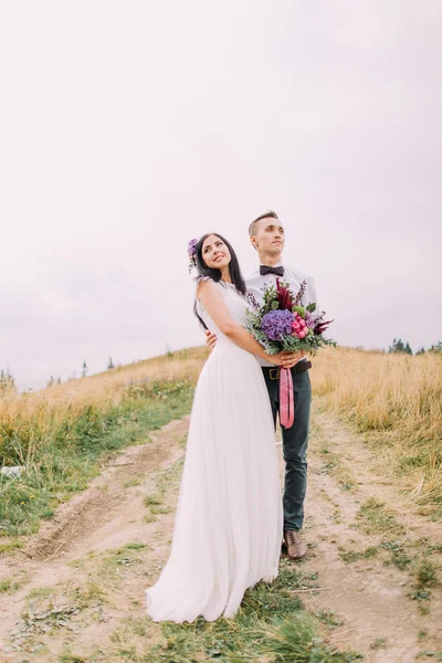 Schönes Hochzeitspaar mit Blumen posiert auf dem Weg in — Stockfoto