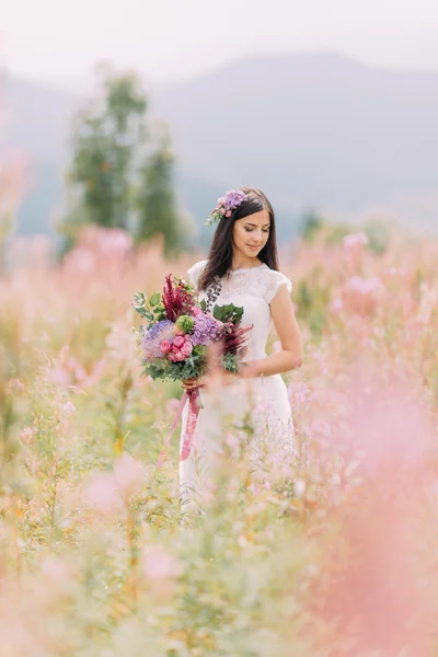 Hermosa novia con flores en el campo. Montañas fondo — Foto de Stock