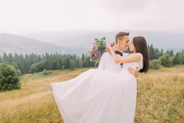 Yakışıklı damat büyüleyici gelini elinde tutar. Dağlar balayı