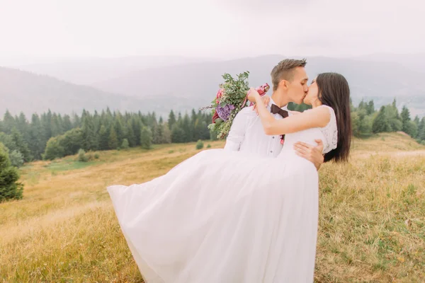 Bello sposo tiene in mano la sua sposa affascinante. Luna di miele in montagna — Foto Stock