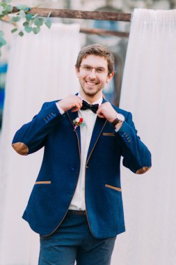 Mutlu bir şekilde gülümseyerek bardaklarda neşeli damat ve onun papyon düzeltir