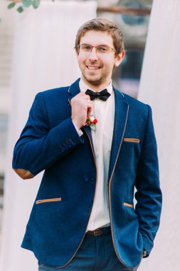 Mutlu damat gülümseyen ve onun papyon düğün arch yakınındaki düzeltir