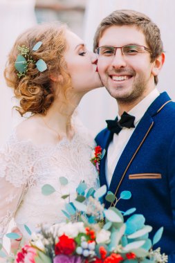 Muhteşem kıvırcık sarışın gelin şefkatle onun gülümseyen damat beyaz arka plan üzerinde öper.