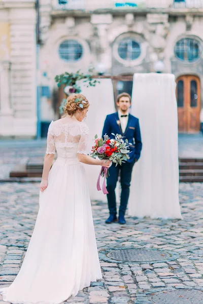 Noiva e noivo lindo elegante posando com buquê de casamento. Arquitetura barroca antiga em segundo plano — Fotografia de Stock