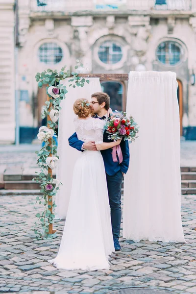 Feliz recién casados besándose suavemente con la vista de la vieja arquitectura europea en el fondo —  Fotos de Stock