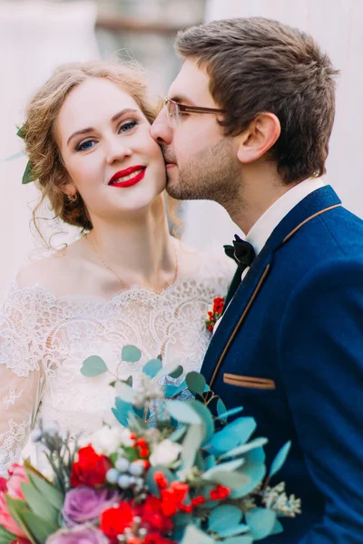 Счастливый жених нежно целует свою удивительную блондинку невесту на белом фоне. — стоковое фото