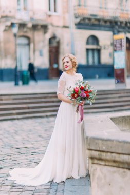 Neşeyle buket el ve arka plan üzerinde antik Lviv mimarisi ile gülümseyen sevimli sarı gelin