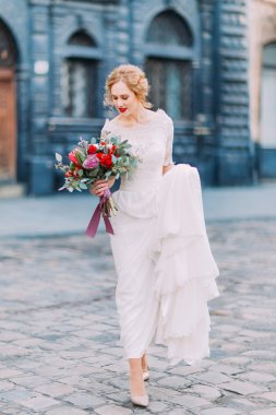 Kıvırcık sarı saçlı güzel gelin incelikle antik Avrupa şehrin sokaklarında yürüyor