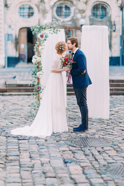 Ceremonia de boda. El novio besa a su encantadora novia en el arco de la boda hábilmente decorado en el fondo —  Fotos de Stock