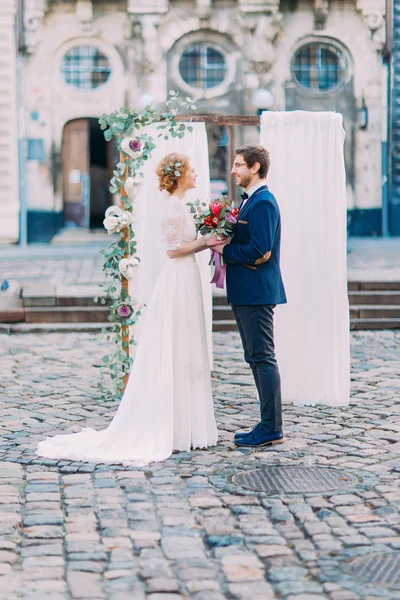 Día de la boda. Novia y novio tomados de la mano cerca del arco de la boda — Foto de Stock