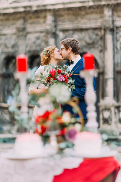 Счастливая свадебная пара целуется с букетом в руках возле винтажного стола — стоковое фото