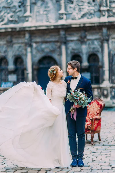 Vacker blond brud i lång spets bröllopsklänning och eleganta brudgummen i glas gärna titta på varandra — Stockfoto