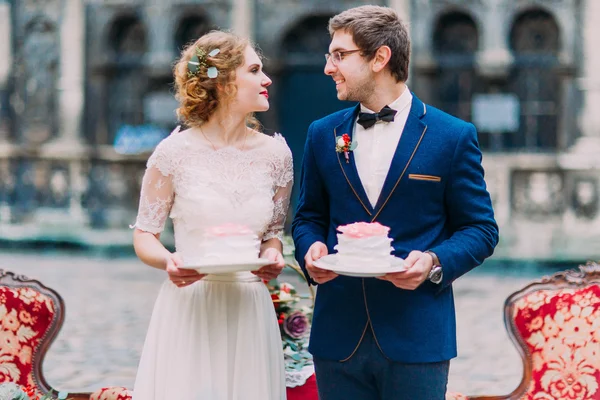 Casamento feliz casal carinhosamente olhar um para o outro com pedaços de bolos de casamento nas mãos — Fotografia de Stock