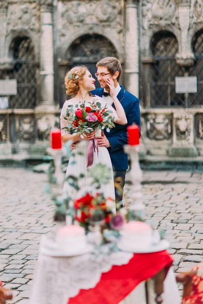 Linda noiva toca suavemente o rosto dos noivos com mesa colorida vermelha e branca vintage com flores e velas em primeiro plano — Fotografia de Stock