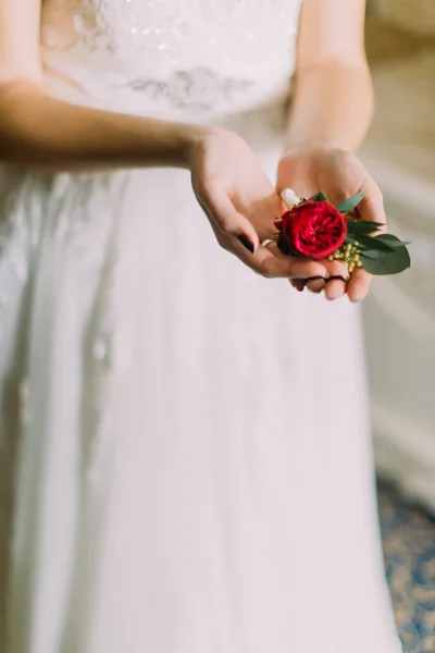Bride in white lace dress holding boutonniere of red rose close up — Stock Photo, Image