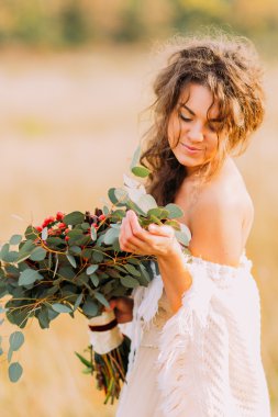 Beyaz elbise tutan buket ve usulca gülümseyen güzel gelin