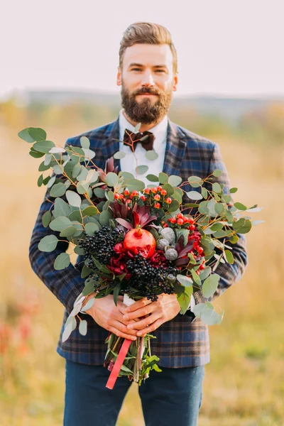 Bebaarde bruidegom met boeket van vruchten op het veld — Stockfoto