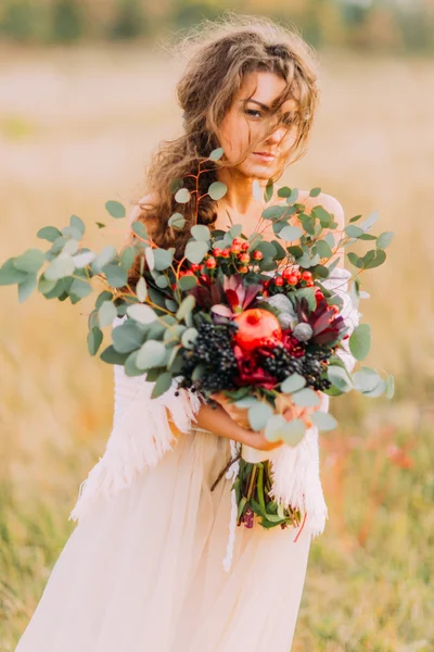 Preciosa novia en vestido étnico blanco sostiene ramo y sonriendo — Foto de Stock