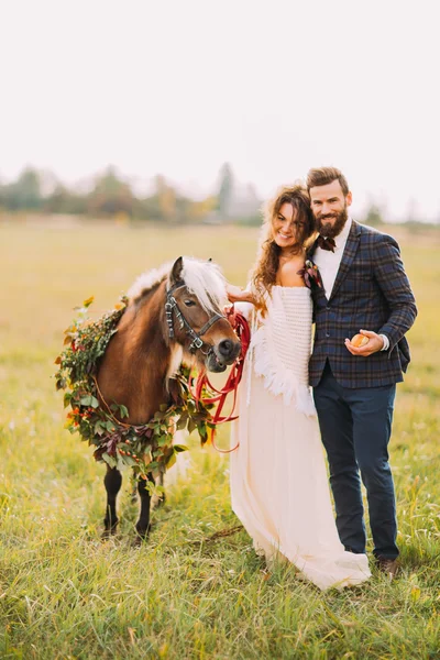 Casal feliz casamento com pônei sorrindo no campo — Fotografia de Stock