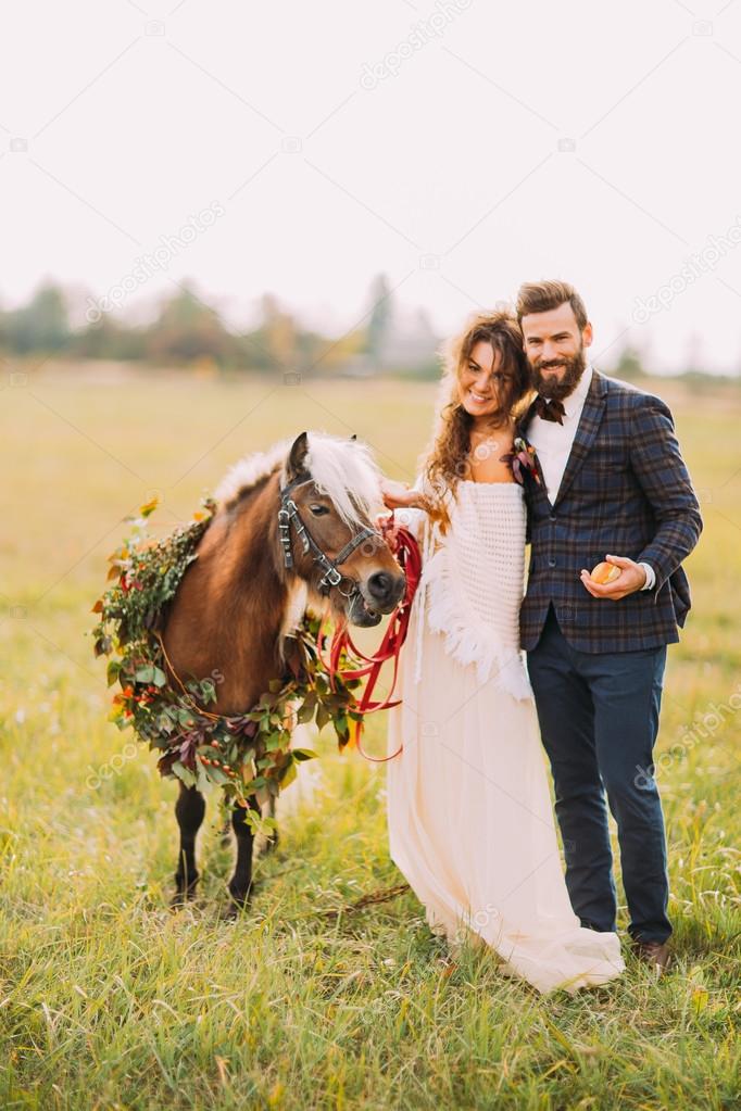 Happy wedding couple with pony smiling on the field