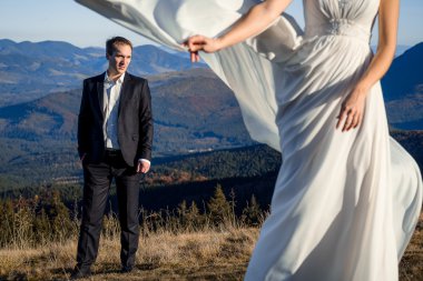 Handsome groom looking at his beatiful bride posing on foreground. Honeymoon in the mountains