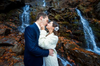 Wedding couple softly hugs on the waterfall. Misty day in mountains