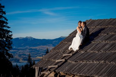 Happy newlyweds sitting on the roof of country house. Honeymoon in mountains