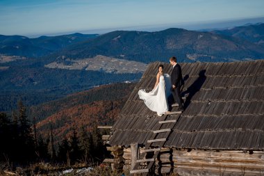 Happy bride and groom on the roof of country house. Breathtaking mountain landscape background.