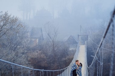 Usulca battaniyeye sarılmış düğün çifti büyüleyici öp dağlar, sospension Köprüsü'nde. Sonbahar Dağları arka plan