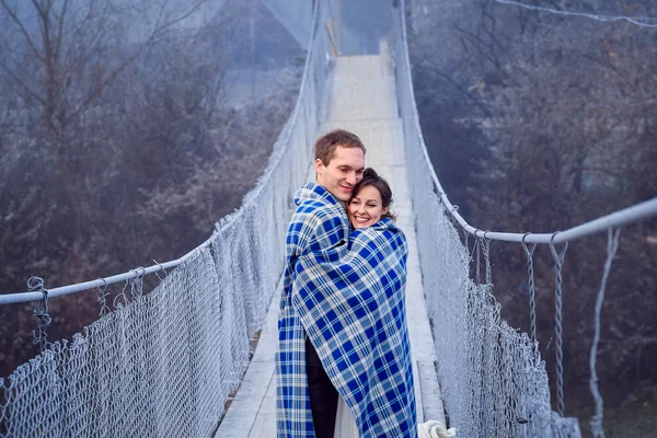 Lovely bride and groom wripped in blanket softly hugs on the wooden bridge. Honeymoon at mountains — Φωτογραφία Αρχείου