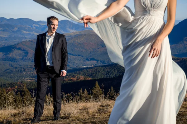 Handsome groom looking at his beatiful bride posing on foreground. Honeymoon in the mountains