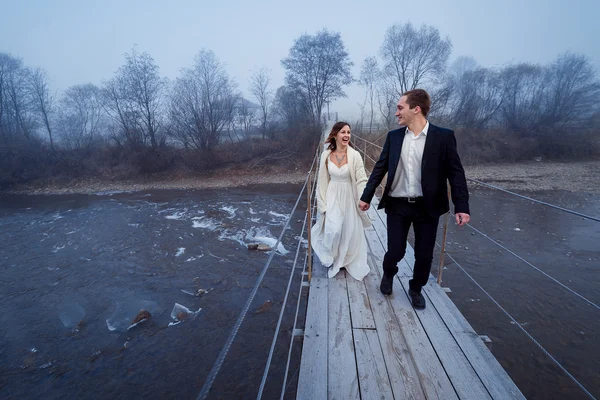 Happy wedding couple laughing and having fun on the suspension bridge in mountains — Stockfoto