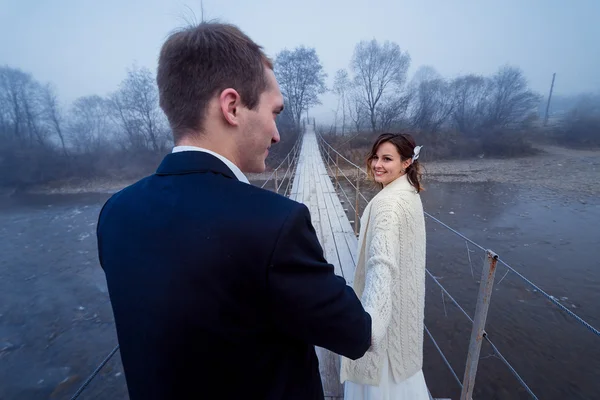 Lovely wedding couple holding hands on the suspension bridge. Honeymoon in mountains — Stock Photo, Image