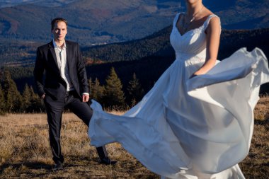Gorgeous bride in white dress dancing before her groom on the mountain peak