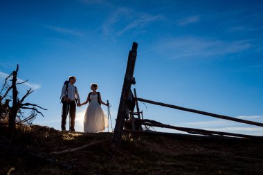Happy newlyweds walking with mountain equipment on the Alpine countryside