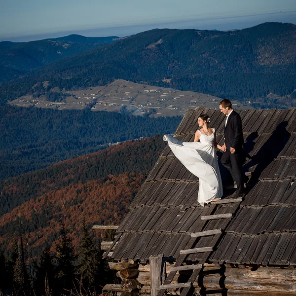 Beautiful wedding couple on the roof of country house. Breathtaking mountain landscape background — Zdjęcie stockowe