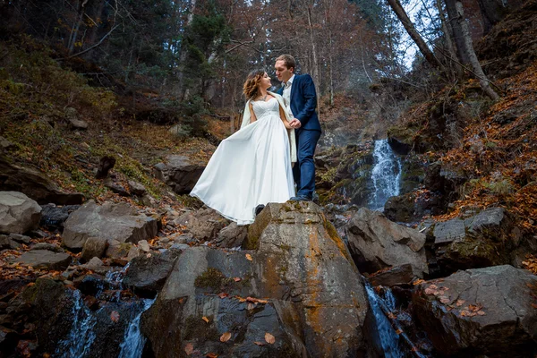 Wedding couple posing on the waterfall. Honeymoon in autumn mountains — Zdjęcie stockowe