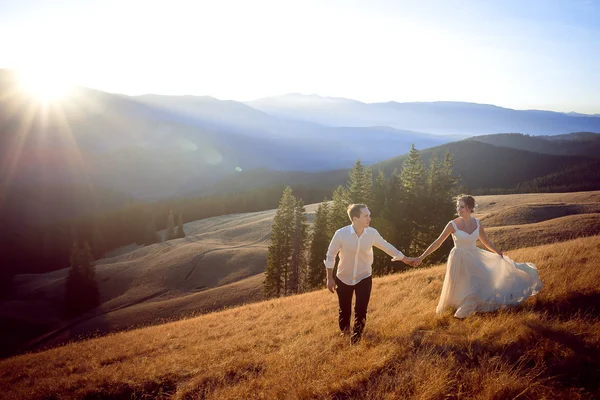Όμορφο γάμο ζευγάρι τρέχει και έχοντας διασκέδαση στο πεδίο που περιβάλλεται από βουνά — Φωτογραφία Αρχείου