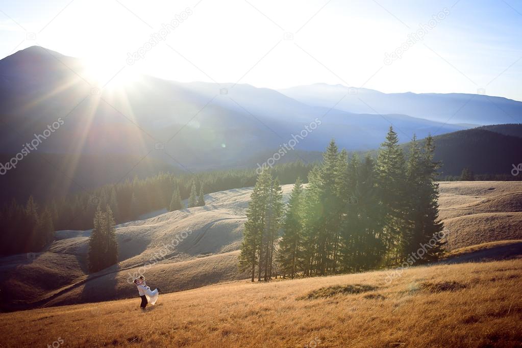Happy groom holds in hands his beautiful bride. Wonderful mountains landscape