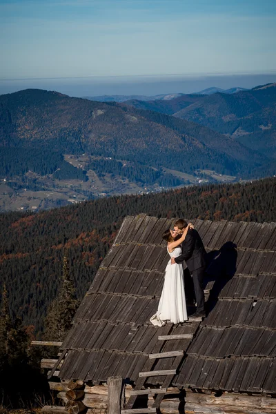 Affascinanti coppie di sposi che si baciano sul tetto della casa di campagna. Incredibile paesaggio di montagna sfondo. Luna di miele — Foto Stock