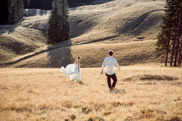 Pareja de bodas corriendo en el campo. Día soleado en las montañas — Foto de Stock