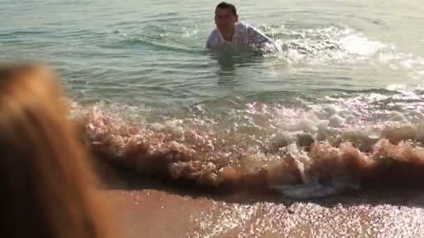 Sexy bruid duwt speels haar bruidegom terug naar de zee door haar breekbare been — Stockvideo