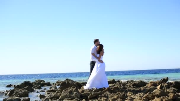 Hermosa pareja de boda se abraza suavemente en la orilla apedreada. Mar sobre fondo . — Vídeos de Stock