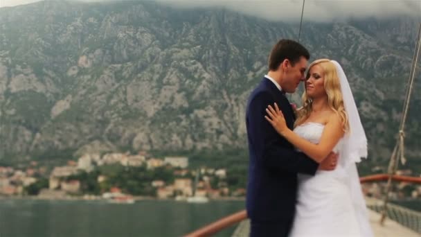 Красивая свадебная пара, держащаяся на яхте с горами и морем на заднем плане — стоковое видео