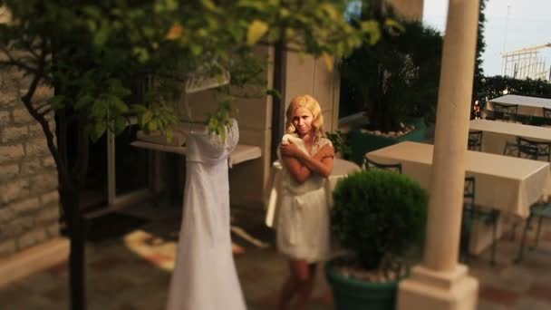 Beautiful blond bride in white robe softly looking on her vintage bridal dress — Stock Video