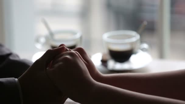 Romantic couple tenderly holding hands. Cups of hot coffee on background — Stock Video