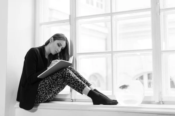 Menina bonita e elegante lendo um livro no peitoril da janela. Foto em preto e branco — Fotografia de Stock