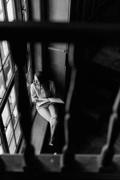 Güzel şık iş kadını bardaklarda pencere üzerine bir kitap okur. Siyah ve beyaz fotoğraf — Stok fotoğraf